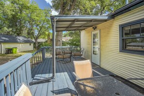 Eine überdachte Terrasse mit Gartenmöbeln, einem Mülleimer und einem Haus mit Fenster und Tür.