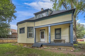 Ein zweistöckiges Haus mit Veranda, Schornstein und kleiner Terrasse.