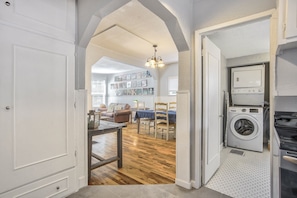 A laundry room with a washing machine and dryer, a dining area with a table and chairs, and a living room with a sofa and a chandelier.
