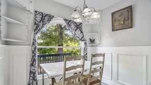 A dining area with a white table and wicker chairs, a chandelier, and a view of greenery outside. - 3bdcheyenne Mtn Suburbsrestaurants & Hiking (Colorado Springs)