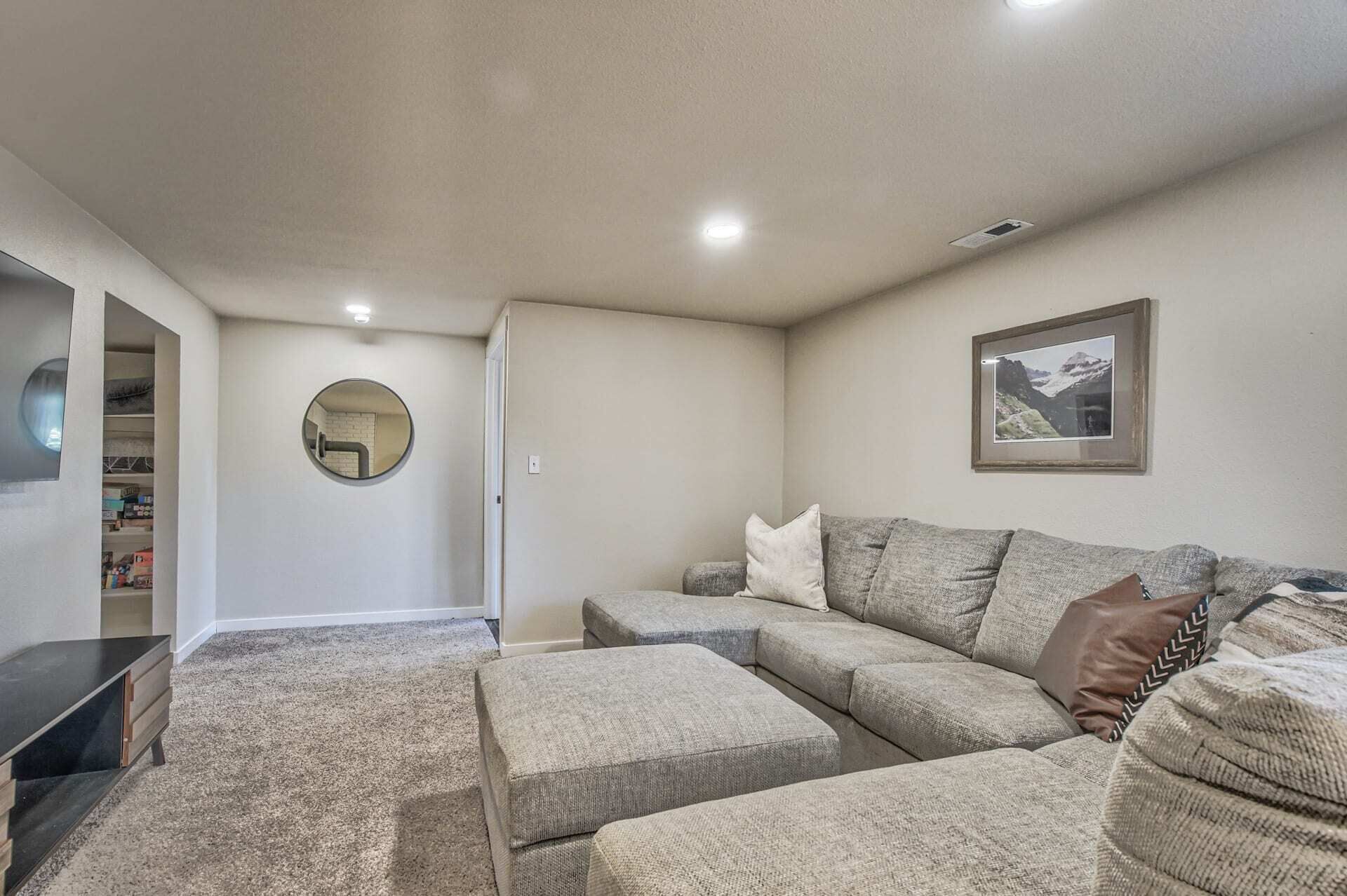 A living room with a sectional sofa, ottomans, a round mirror, and a framed picture on the wall.