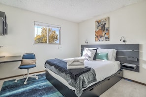 A modern bedroom with a bed, desk, chair, and artwork.