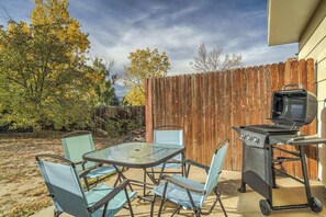 An outdoor patio with a glass table and chairs, a barbecue grill, and a wooden fence.