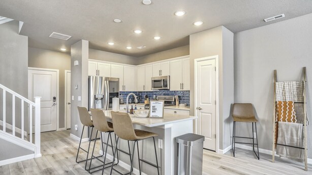 A modern kitchen with white cabinets, stainless steel appliances, and a bar area with stools. - 3BD Modern Home Close to Usafa (Monument)