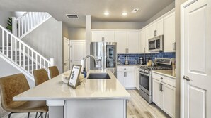 A modern kitchen with white cabinets, stainless steel appliances, and a central island with seating. - 3BD Modern Home Close to Usafa (Monument)