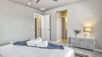 Quarto com cama, ventilador de teto, mesa de cabeceira com abajur e cômoda.