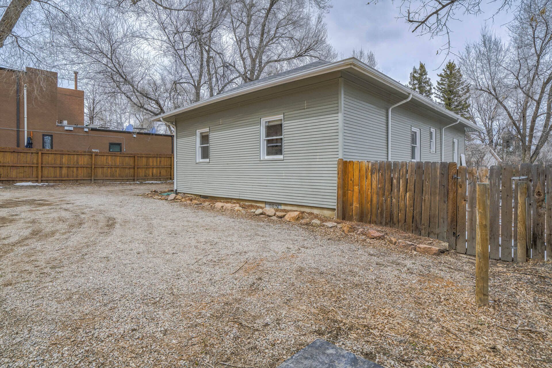 A single-story house with a gravel driveway, a wooden fence, and a wooden deck.