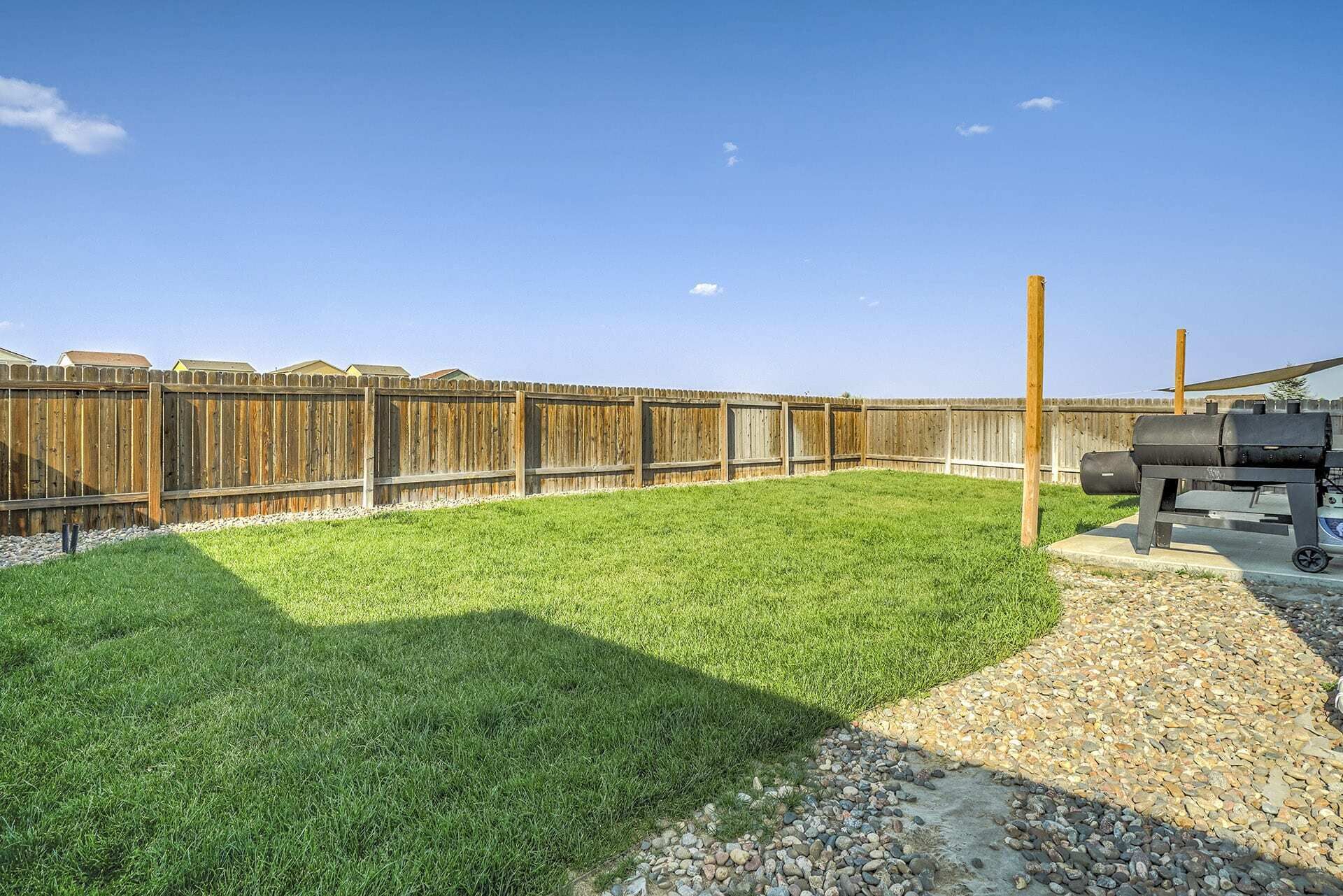 Un jardin avec une clôture en bois, un barbecue et un chemin de gravier.