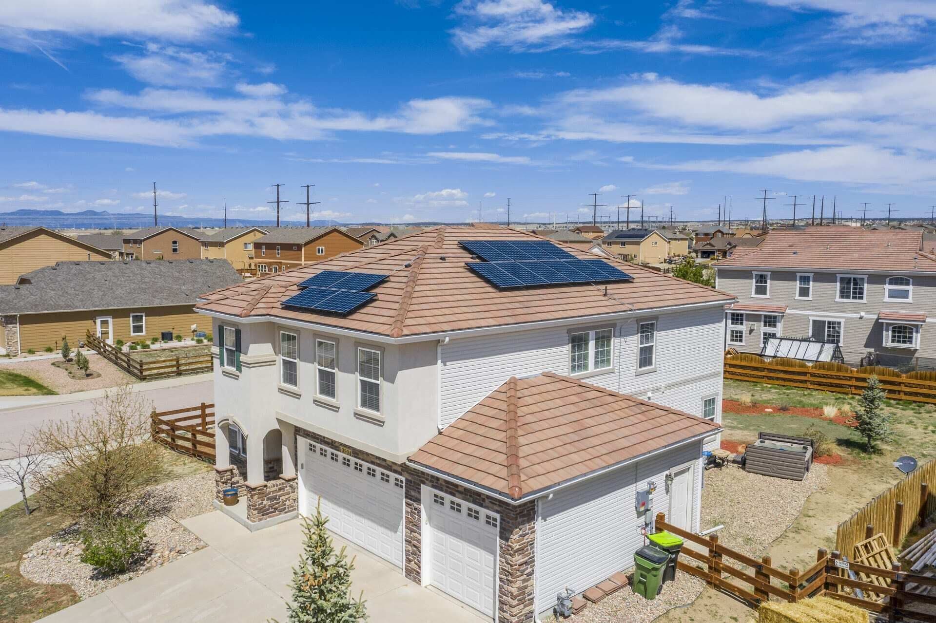 A residential building with solar panels on the roof, a garage, and a fenced yard.