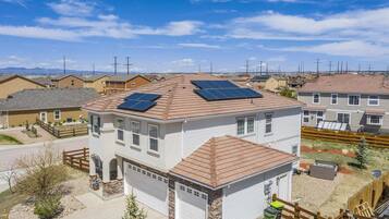 A residential building with solar panels on the roof, a garage, and a fenced yard.