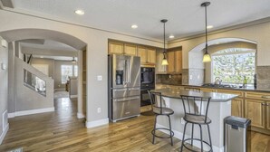 A modern kitchen with stainless steel appliances, wooden cabinets, and a bar area with stools.