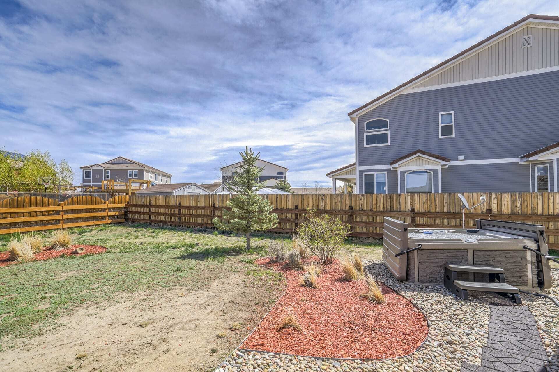 A residential backyard with a wooden fence, a small tree, and a barbecue area.