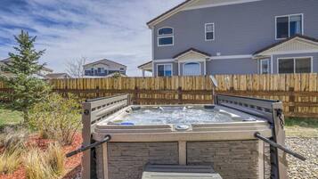 A hot tub in a backyard with a wooden fence, stone wall, and a house in the background.