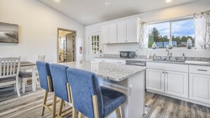 Une cuisine moderne avec des meubles blancs, un plan de travail en granit et une grande fenêtre agrémentée de rideaux.