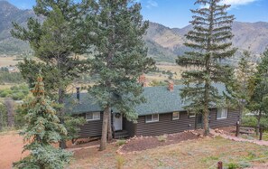 A log cabin with a green roof, surrounded by tall pine trees and mountains in the background. - 3BD Cowboy Cabin Pikes Peak Mountain Log Cabin (Cascade)