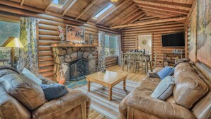 Un acogedor interior de cabaña de madera con chimenea de piedra, sofás de cuero, comedor y televisor.
