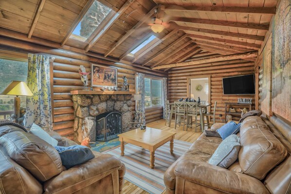 A cozy log cabin interior with a stone fireplace, leather sofas, a dining area, and a television. - 3BD Cowboy Cabin Pikes Peak Mountain Log Cabin (Cascade)