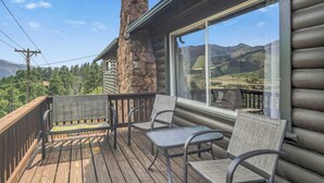Una terraza de madera con mobiliario exterior y un ventanal con vistas a un paisaje montañoso.