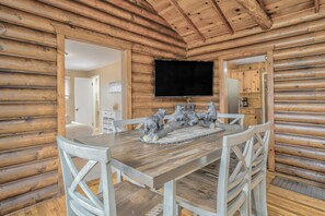 A wooden cabin interior with a dining table, chairs, a flat-screen TV, and a bear sculpture centerpiece. - 3BD Cowboy Cabin Pikes Peak Mountain Log Cabin (Cascade)