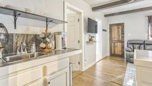 A kitchen with a marble backsplash, stainless steel sink, and a coffee machine. There is a wooden door leading to a living area with a leather couch. - 2BD Cozy Retreatclose to Red Rocksdogs Welcome! (Colorado Springs)