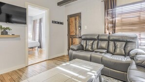 A living room with a leather sofa, a flat-screen TV mounted on the wall, a wooden coffee table, and a door leading to another room. - 2BD Cozy Retreatclose to Red Rocksdogs Welcome! (Colorado Springs)