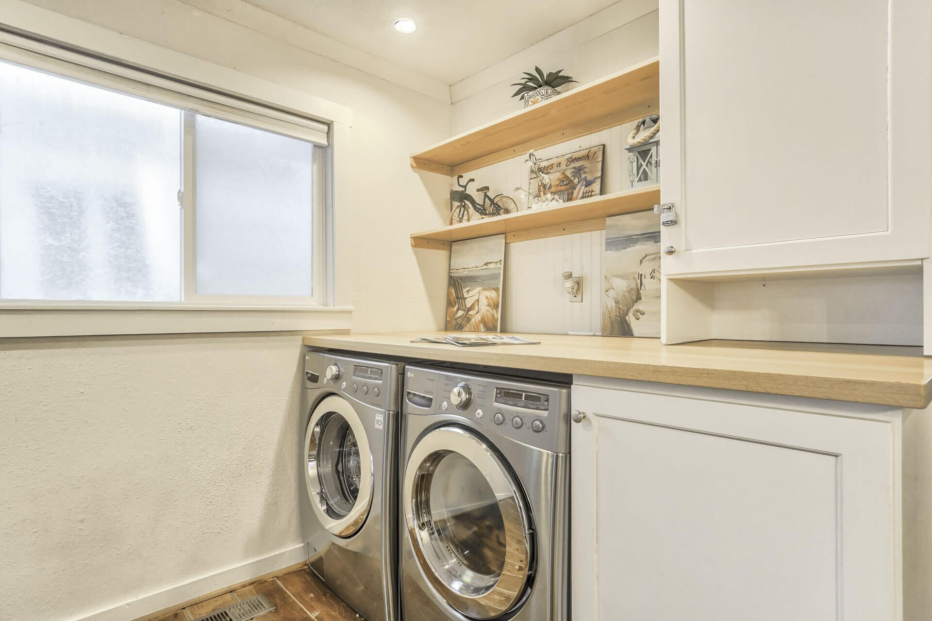 A compact laundry room with two front-loading washing machines, a window with frosted glass, and a shelf with decorative items.