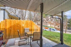 Un patio techado con cerramiento de madera, mobiliario exterior y vista a una calle residencial.