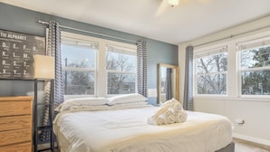 A bedroom with a large bed, a dresser, a mirror, and a window with curtains.