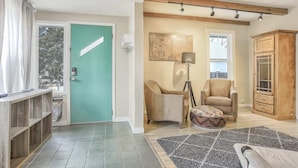 A room with a teal door, a wooden cabinet, a chair, a floor lamp, and a patterned rug.