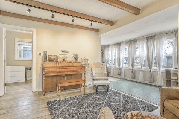 Amplia sala de estar con un piano de madera, un sillón cómodo y un ventanal con cortinas.
