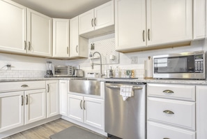 Una cocina con gabinetes blancos, electrodomésticos de acero inoxidable, lavavajillas y microondas.