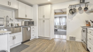 A modern kitchen with white cabinets, stainless steel appliances, and a wooden floor.