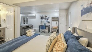 Quarto de hotel com cama, escrivaninha e cadeira. Um banheiro é visível ao fundo.