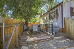 A covered patio area with a brick floor, metal chairs, and a wooden fence. - 1BD Suitewalking Distance From Red Rocks (Colorado Springs)