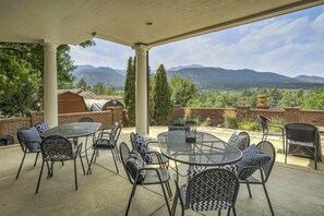 An outdoor patio with round tables and chairs, a brick wall, and a view of mountains. - Broadmoor Luxury Mansion 5 Star Experience Theater Cheyenne Mountain Views (Colorado Springs)