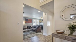 A spacious living room with a fireplace, a dining area, and a hallway leading to a bedroom.