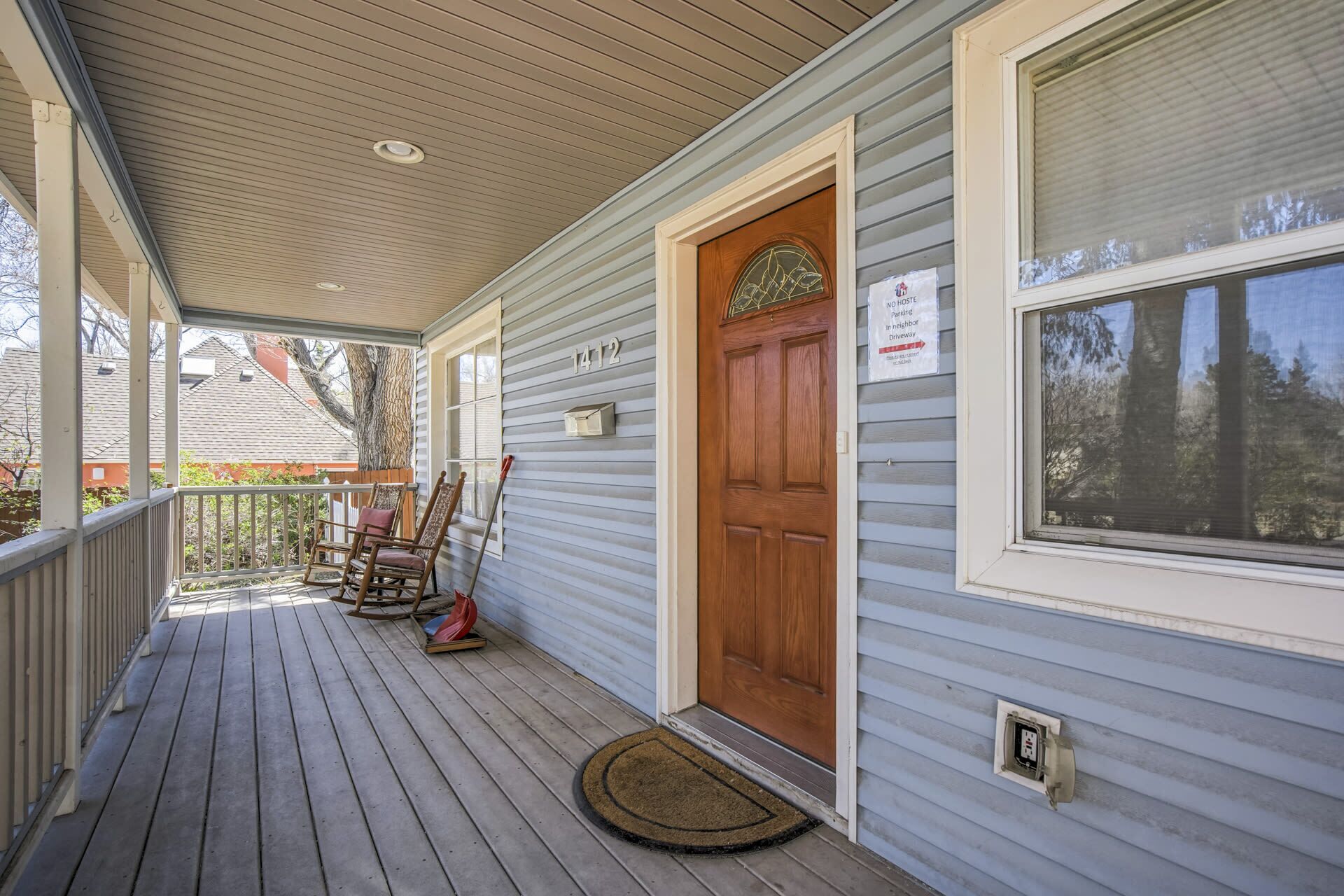 A covered porch with a wooden door, a window, and a sign indicating no hosteling parking.