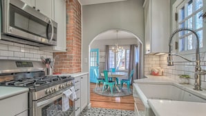 A kitchen with a gas stove, microwave, and modern cabinetry. There is a dining area with a round table and chairs, and a brick wall. - 1bdlovely Cottagedogs Welcome!near Olympic Training Center (Colorado Springs)