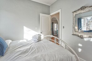 Ein Schlafzimmer mit einem Bett, einem Stapel Handtüchern, einer weißen Tür und einem Spiegel mit dekorativem Rahmen.