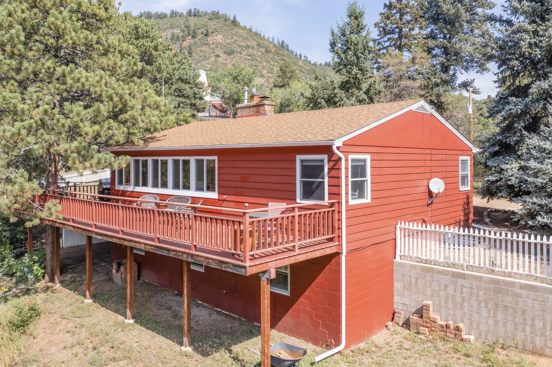 Une maison en bois rouge avec un balcon, entourée d’arbres et avec une colline en arrière-plan.