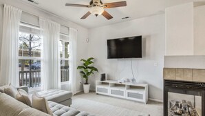 Un salon avec un canapé gris, un téléviseur fixé au mur, une cheminée et un ventilateur de plafond.