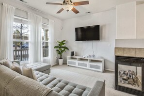 Una sala de estar con un sofá gris, un televisor montado en la pared, una chimenea y un ventilador de techo.
