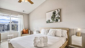 Une chambre d’hôtel avec un grand lit, une table de chevet avec une lampe, une fenêtre avec des rideaux et une plante fixée au mur.