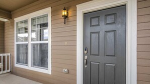 Une maison avec une porte d’entrée grise, une fenêtre à cadre blanc et un luminaire fixé au mur.