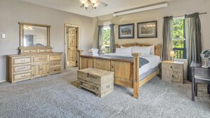 A bedroom with a wooden bed, a dresser, a chest of drawers, a desk, and a ceiling fan.