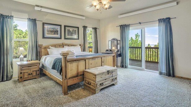 A bedroom with a wooden bed, a nightstand, a chest of drawers, a ceiling fan, and a view of the outdoors through a sliding glass door.
