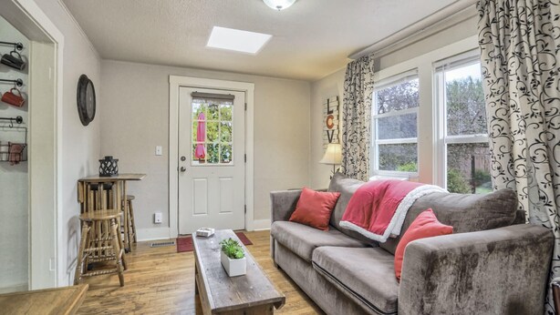A cozy living room with a grey sofa, a wooden coffee table, and a window with patterned curtains.