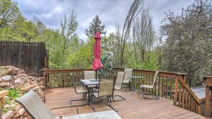 A wooden deck with outdoor furniture, including chairs and a table, surrounded by a wooden fence and trees.