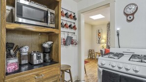A kitchen with a microwave, toaster, and stove. There are hanging pots and pans, and a clock on the wall.