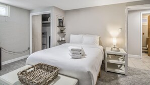 A hotel room with a bed, a bedside table with a lamp, a small shelf with toiletries, a wicker basket, and a closet with shelves. - 5BR 💖heart Of Old Colorado Cityfoosball 💖 (Colorado Springs)